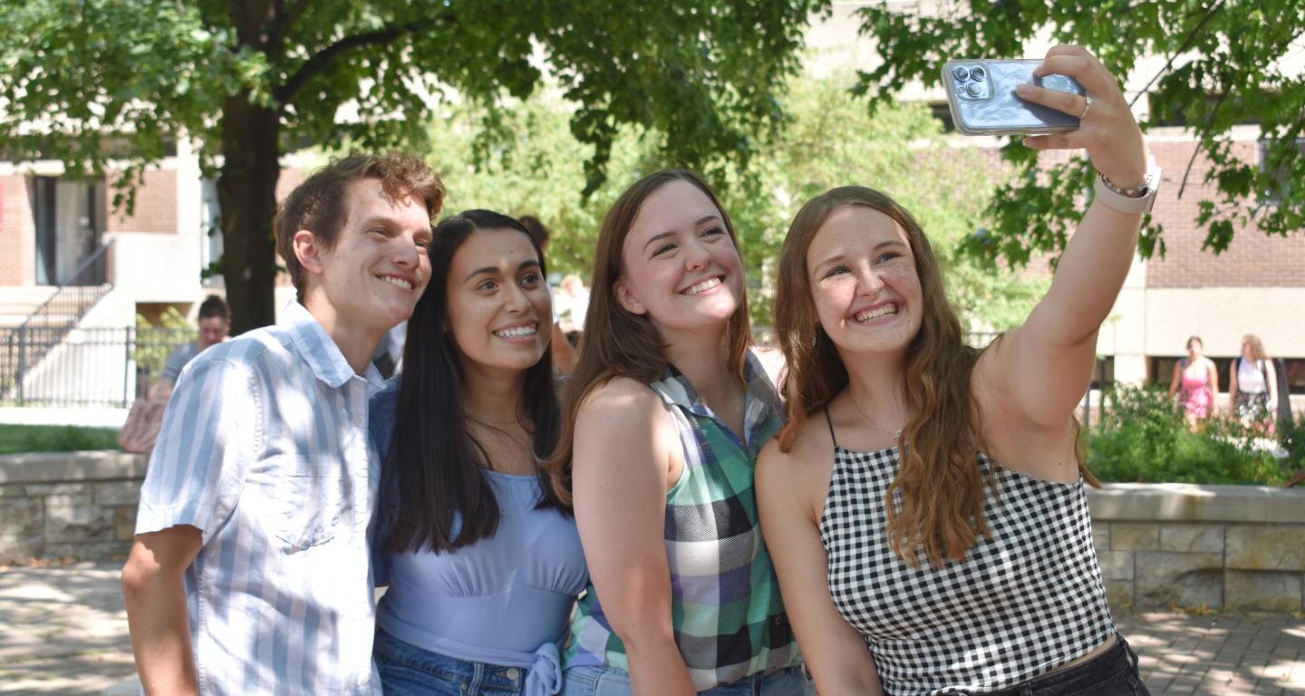 Four students are posing for a selfie outside on campus.